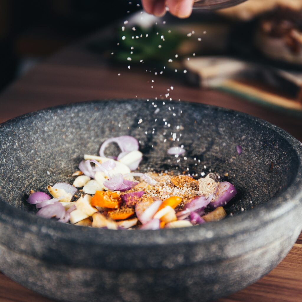 Close-up of seasoning being added to fresh ingredients in a stone bowl, perfect for culinary themes.