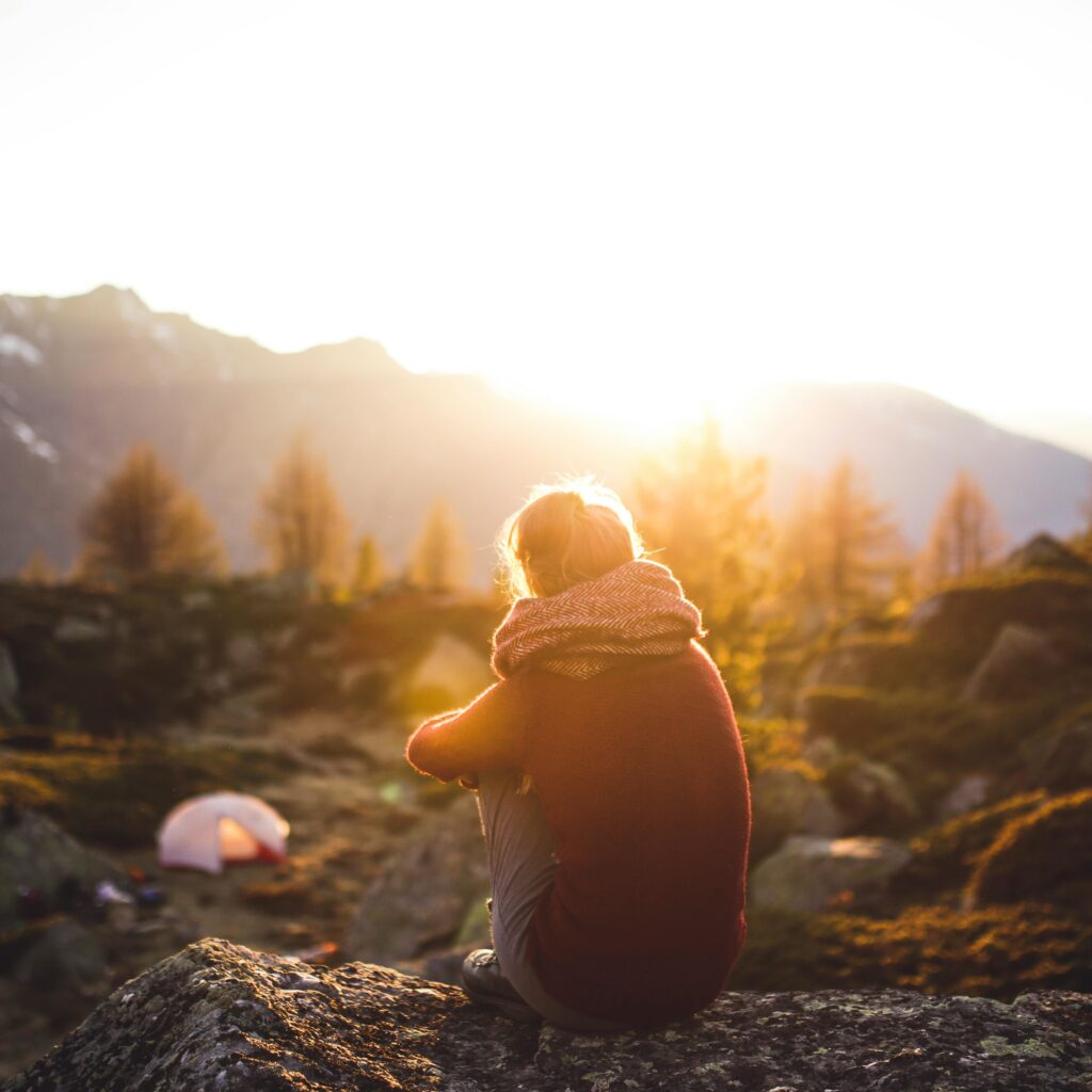 A woman sits on a rock enjoying the serene mountain view at sunrise in Sachseln, Switzerland.